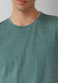 Grünes meliertes Rundhals-T-Shirt, hergestellt aus leichtem Stoff mit einer weichen Textur, mit einem schlichten Design und einem lässigen Schnitt.