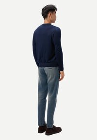 Marineblauer Pullover aus weichem Strickmaterial mit klassischem Design, Rundhalsausschnitt und geripptem Saum, kombiniert mit verblassten blauen Jeans.