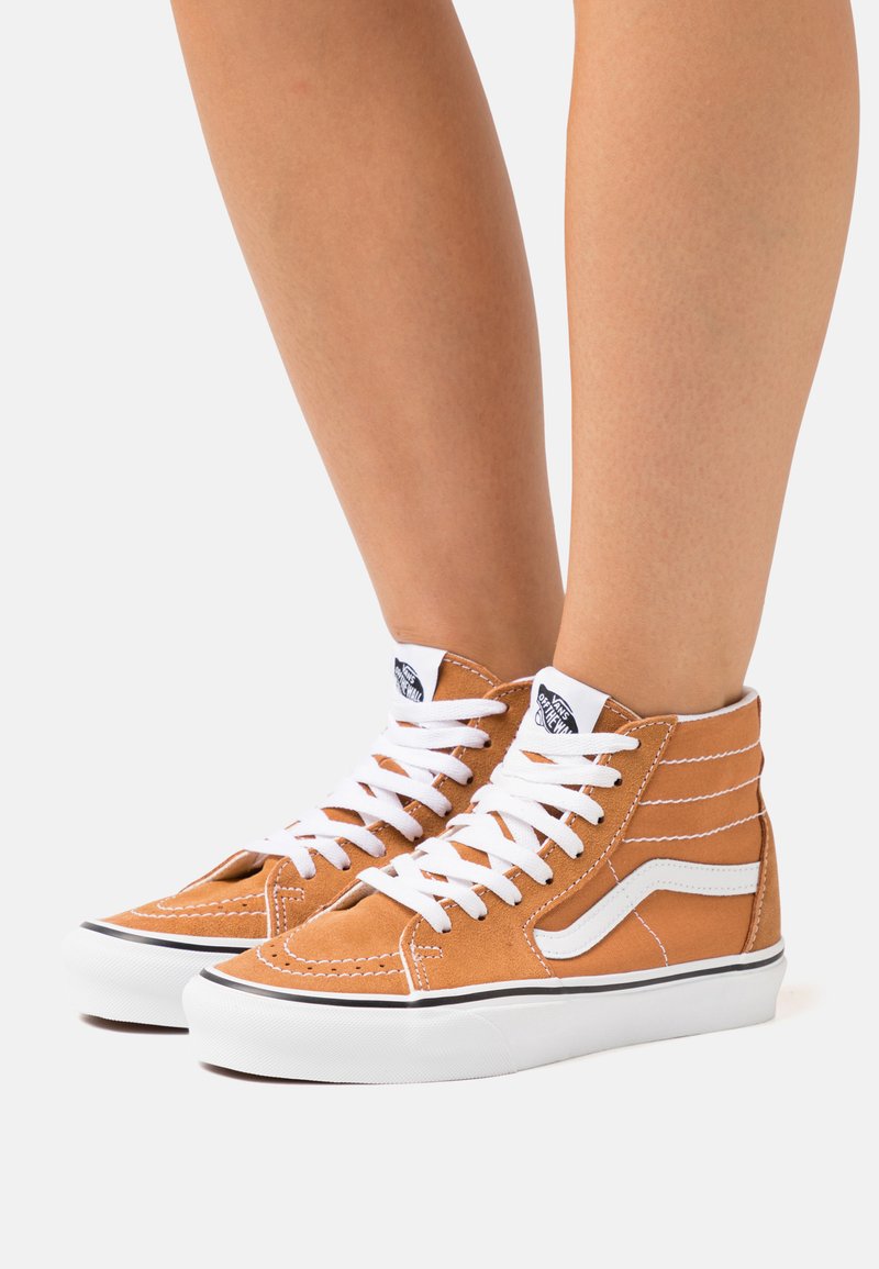 Zapatillas altas de ante en color marrón claro con acentos en blanco, que cuentan con un collar acolchado, cordones blancos y una etiqueta de logo negra en la lengüeta.