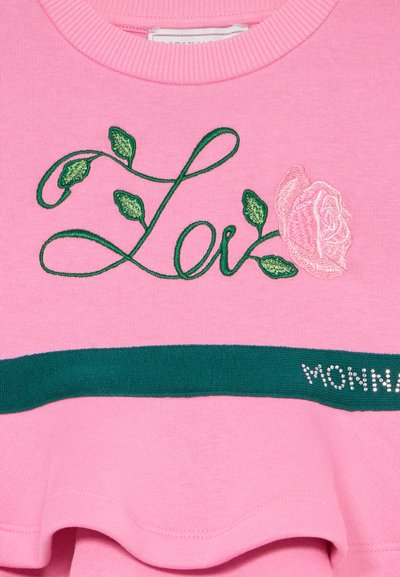 Rosa Stoff mit grünem, gesticktem Wort "Liebe", versehen mit Blattdetails und einer rosa gestickten Rose, über einem grünen Streifen mit teilweise sichtbarem Text.