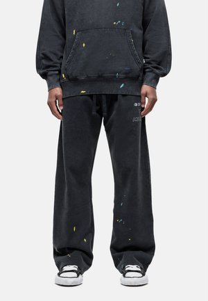 Zwarte oversized hoodie en bijpassende broek met verfspetters in geel, blauw en groen. De broek heeft een elastische tailleband en een relaxte pasvorm.