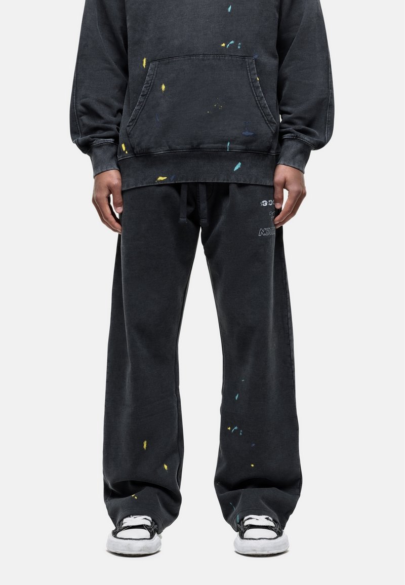 Zwarte oversized hoodie en bijpassende broek met verfspetters in geel, blauw en groen. De broek heeft een elastische tailleband en een relaxte pasvorm.