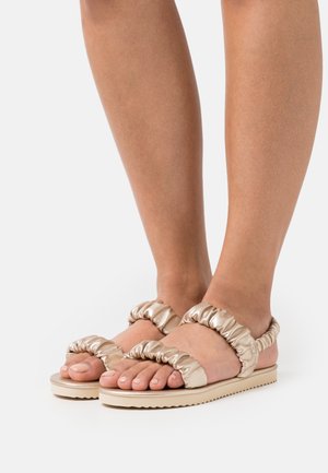 Light gold sandals with ruched strap design, flat sole, and textured detailing. Open-toe style with minimalistic and modern aesthetics.