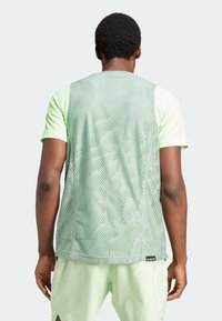 Top deportivo de color verde claro con textura de malla y patrones sutiles, mostrado desde atrás. Combinado con pantalones cortos a juego de color verde claro.