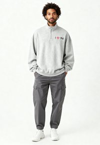 Sweat-shirt en polaire grise avec fermeture éclair quart et broderie "I ❤️ YOU". Associé à un pantalon cargo gris ample et des baskets blanches.