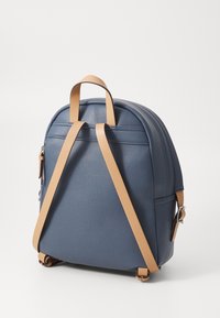 Niebieski skórzany plecak z dwoma regulowanymi paskami w kolorze jasnobrązowym, zaokrąglonym górnym połacią, przednią kieszenią na suwak i teksturowaną powierzchnią. Prosty i funkcjonalny design.