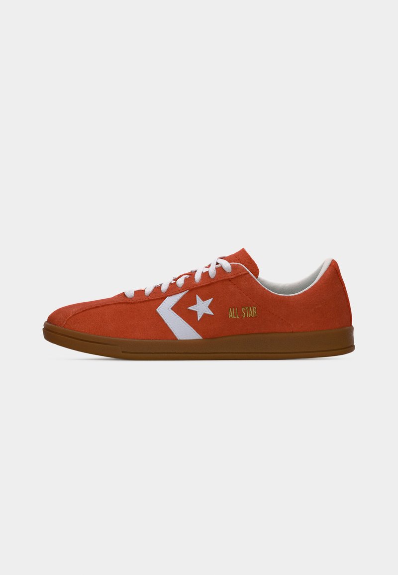 Zapatilla de perfil bajo en ante rojo con cordones blancos, logo de estrella blanca, texto amarillo "All Star" y suela de goma marrón, vista lateral.