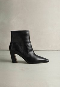 Zwarte leren enkelboot met een spitse neus, textuur op het oppervlak en een blokhakontwerp. De zool lijkt glad met minimale accentdetails.