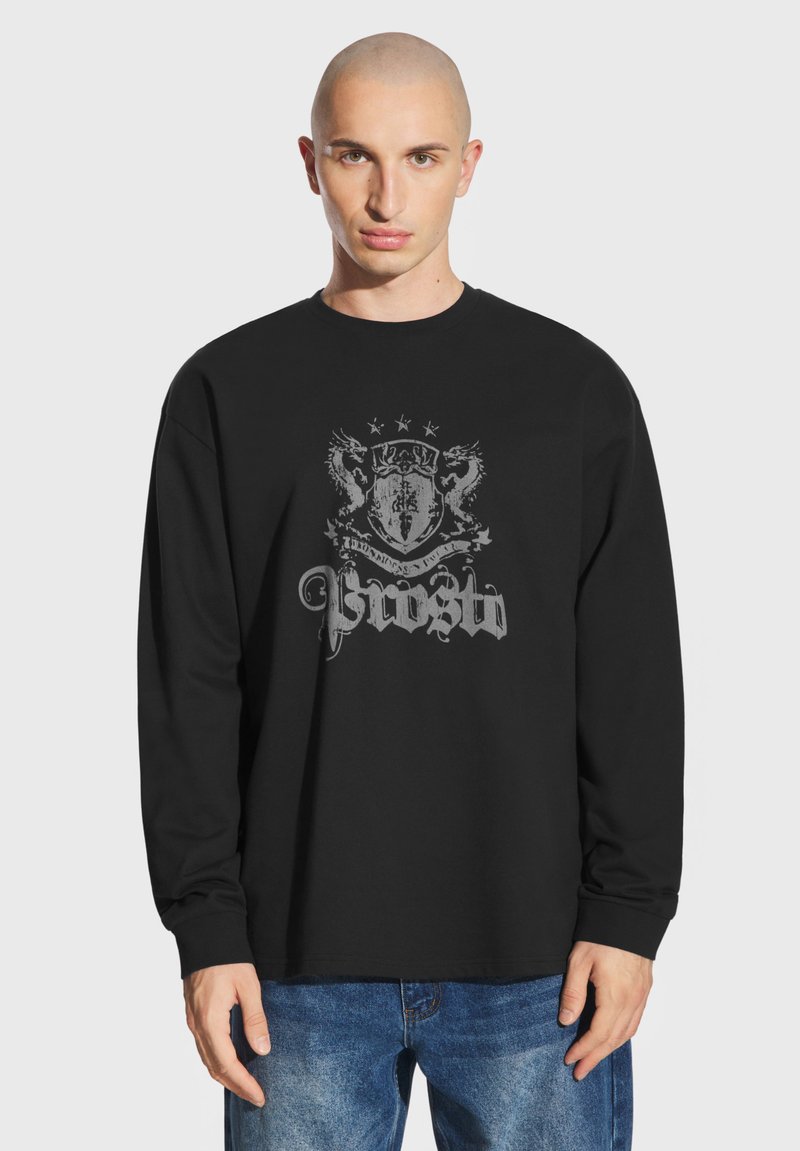 Czarny longsleeve z długim rękawem z szarym wzorem graficznym przedstawiającym tarczę i smoki, wykonany z bawełny, w standardowym kroju, z okrągłym dekoltem i prążkowanymi mankietami.