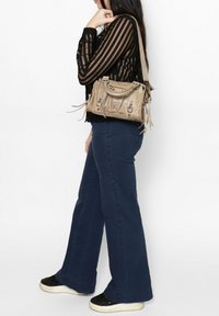 Borsa beige con finitura texturizzata, dettagli in metallo e tracolla, abbinata a jeans svasati blu scuro e sneakers nere.