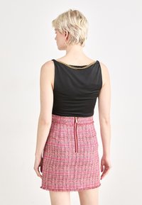 Musta ilmanhiha toppi, jossa on kultaketju korostus kaula-aukossa, yhdistettynä pinkkiin teksturoituun tweed-hameeseen, jossa on keskimmäinen vetoketju.