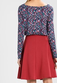Top de manga larga con fondo azul marino, decorado con patrones en rosa y verde; combinado con una falda A-line roja sólida, de largo hasta la rodilla.