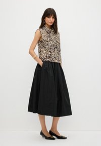 Luipaardprint mouwloze top, zwarte geplooide rok en zwarte kitten heels met gouden accenten. Glad stof, op maat gemaakte pasvorm en zijkanten met zakken.