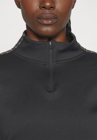 Zwarte pullover met hoge kraag en een halve ritssluiting, met subtiele textuurdetails langs de kraag voor extra visuele interesse.