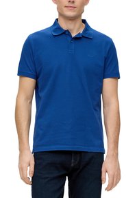 Polo blu realizzato in cotone, con colletto, maniche corte e un logo sul lato sinistro del petto. Indossato con jeans di jeans scuri.
