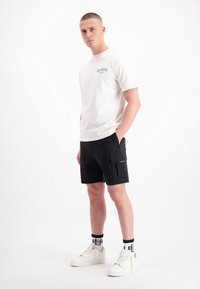 Witte T-shirt met een kleine graphic, zwarte cargoshorts met zakken, witte sneakers en zwart-witte gestreepte sokken. Schoon, casual uiterlijk.