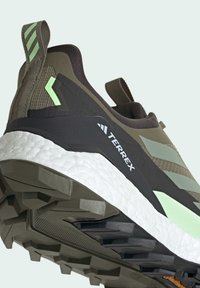 Zapatilla de running Terrex en verde oliva y negro con amortiguación blanca. Presenta un tejido texturizado, acentos angulares y un patrón de suela resistente.