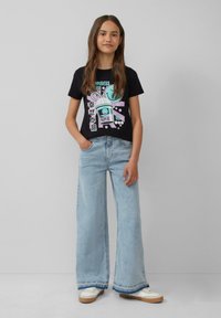 Zwarte graphic t-shirt met kleurrijk ontwerp van een konijn en tekst, gecombineerd met lichtblauwe wijde jeans en witte sneakers.