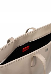 Borsa tote in pelle beige con doppio manico, con un interno nero a contrasto. Include un patch con logo rosso e dettagli in hardware argentato.