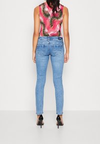 Blå denimjeans med slim fit, med bakfickor och subtila sömnadsdetaljer. Matchas med en ärmlös rosa topp med palmbladsmönster.
