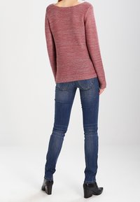 Pull en tricot bordeaux clair avec un décolleté large, associé à un jean foncé ajusté et des bottines à talons noires, vu de dos.