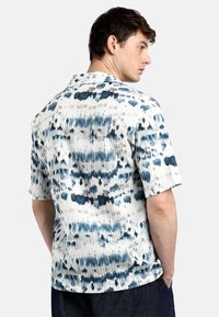 Camicia a maniche corte realizzata in tessuto bianco con motivi astratti blu e grigi, design a coste testurizzate e colletto classico piatto.