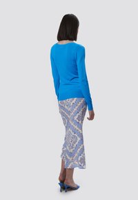 Blauer Strickpullover mit langen Ärmeln, kombiniert mit einem gemusterten hellblauen Rock mit Paisley-Muster. Blaue Absatzmules runden das Outfit ab.