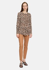 Blusa con stampa leopardata a maniche lunghe, dettagli plissettati sul davanti, abbinata a pantaloni beige aderenti e tacchi neri con cinturino.