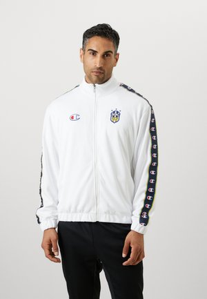 Veste blanche zippée avec col montant, comporte un logo et des détails en bandes multicolores sur les manches, fabriquée en tissu lisse et léger.