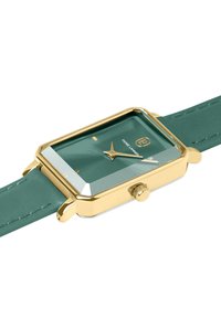 Green rectangular watch with gold-tone case, mineral glass, and green leather strap. Features gold hands and brand logo on the dial.