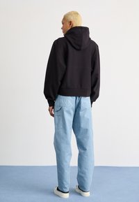 Black cropped hoodie with a large hood and loose fit, paired with light blue wide-leg cargo pants featuring side pockets.