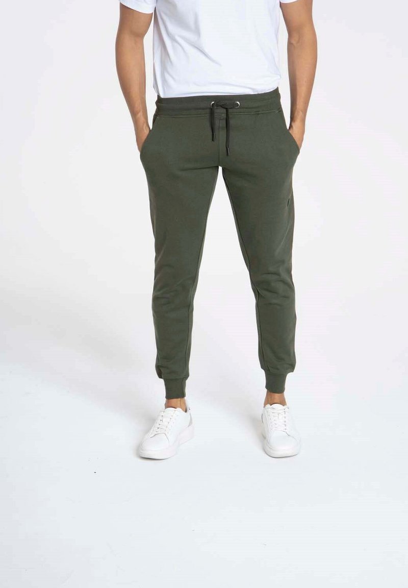 Pantalons de jogging verts en tissu doux avec un waistband élastique, des poches latérales et des poignets côtelés, associés à des baskets blanches.