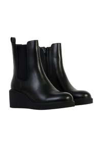 Paire de bottines compensées en cuir noir avec fermeture à glissière latérale et panneau élastique sur fond blanc.