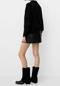 Suéter negro de punto, falda mini de cuero y botas negras de caña alta con textura de canalé. Los detalles incluyen puños de canalé y una silueta ajustada.