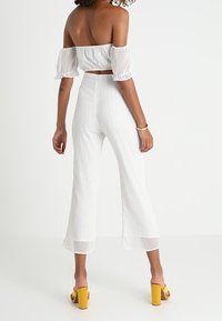 Biały króki top na ramiączkach z bufiastymi rękawami w komplecie z białymi spodniami w paski o wysokim stanie. Żółte platformy dopełniają całość.