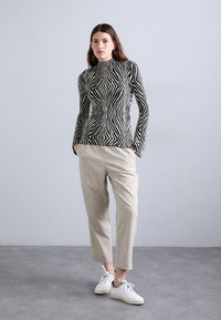 Suéter de punto de cuello alto a rayas en blanco y negro con un diseño ajustado, combinado con pantalones beige claros de corte entallado y zapatillas blancas.