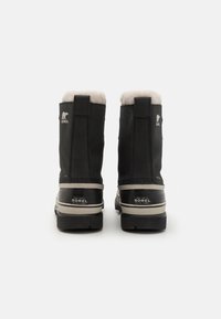Zwarte waterdichte winterlaarzen met een pluizige witte bontvoering, versterkte hak en beige buitenzool met "SOREL" branding aan de achterkant.