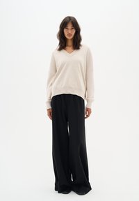 Pull en V beige avec des épaules tombantes, associé à un pantalon wide-leg noir taille haute. Texture douce, design minimaliste.
