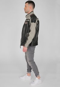 Svart och grå läderjacka med dragkedja framtill, racingränder, vadderade axlar och en logopatch, kombinerad med grå jeans och vita sneakers.