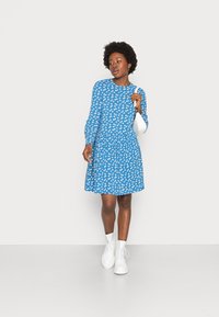 Vestido azul com padrão floral branco, decote redondo, mangas longas e saia godê. Combinado com botas brancas até o tornozelo. Design simples e elegante.