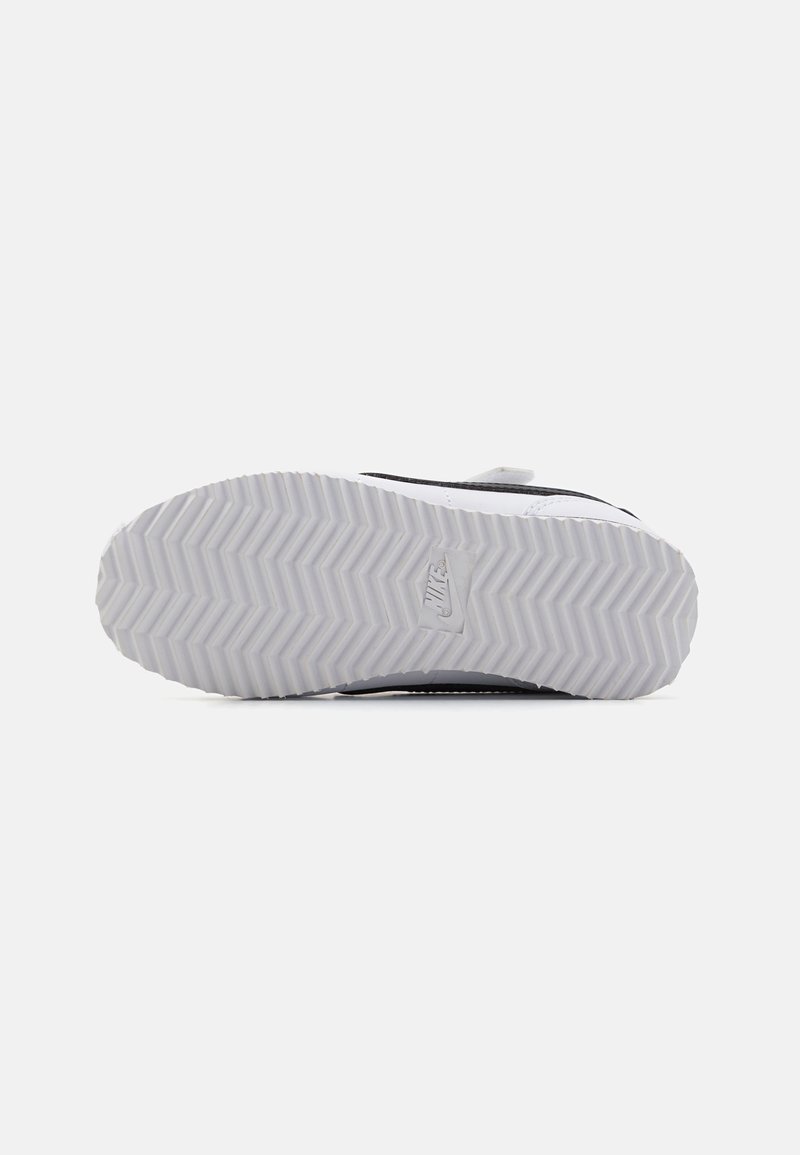 Suela de zapato Nike con un patrón de tracción en espiga en gris claro. Parte superior en negro y blanco, con una forma redondeada y un acabado texturizado.
