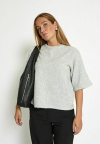 Light grey, textured, loose-fitting sweater with short sleeves; worn with black pants and a large black leather bag featuring a zip.