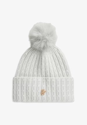 Hvid strikket vinters hat med kvast på toppen og et lille gyldent dekorativt emblem på den foldede kant.