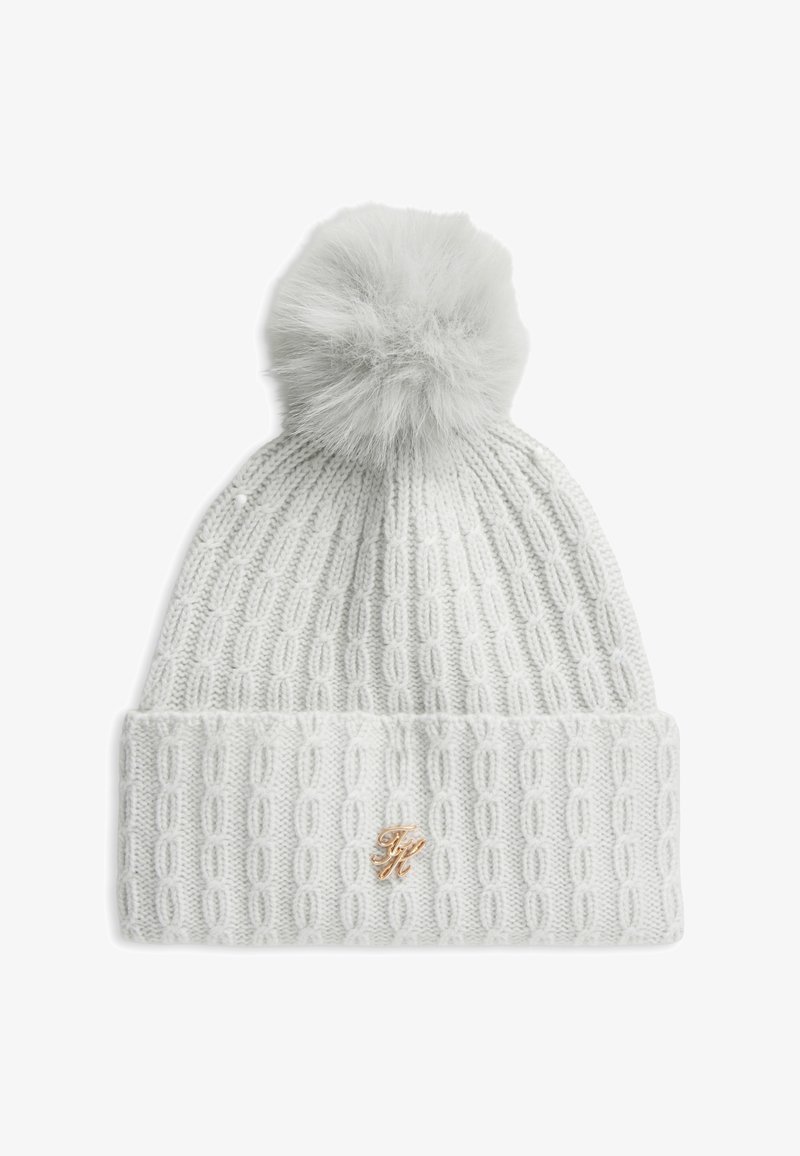 Bonnet d'hiver blanc en maille avec un pompon sur le dessus et un petit emblème décoratif doré sur le revers.