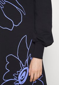 Vestito di stoffa nera con un grande motivo floreale azzurro, con maniche arricciate e polsini aderenti. Texture liscia.