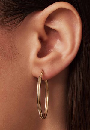 Goldene Creolen, Doppellinien-Design mit glatter, glänzender Oberfläche. Hängen von einem kleinen Verschluss und werden in einem Nahaufnahme eines Ohres getragen.