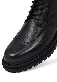 Zwarte leren brogueboot met gedetailleerde perforaties, gegrofde bovenkant, traditionele vetersluiting en robuuste zool voor verbeterde grip.