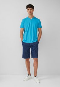 Męska koszulka polo z krótkim rękawem w kolorze turkusowym z dekoltem w serek, w połączeniu z ciemnoniebieskimi szortami dżinsowymi i białymi sneakersami. Gładka, jednolita tekstura.