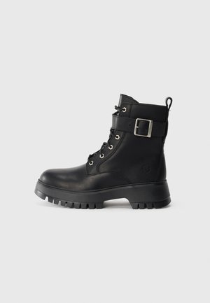 Botte de combat en cuir noir avec semelle en caoutchouc épaisse, devant à lacets, sangle à la cheville avec boucle en argent et languette à l'arrière.