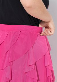 Falda rosa con volantes, elaborada en tela ligera con un diseño en capas. Presenta una cinturilla ancha y una textura suave. Vista en primer plano desde un lado.